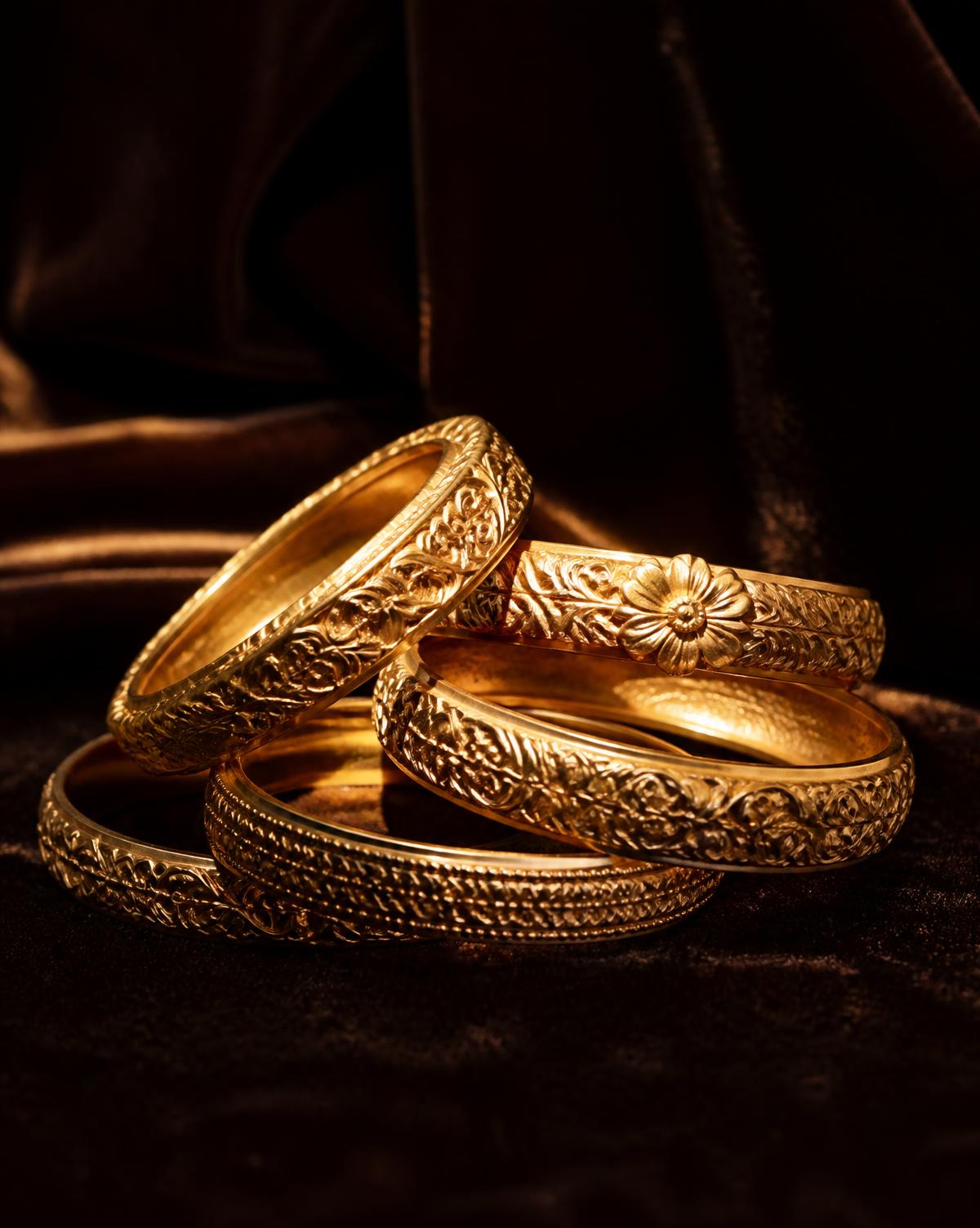 Stack of ornately carved gold bangles on dark espresso velvet