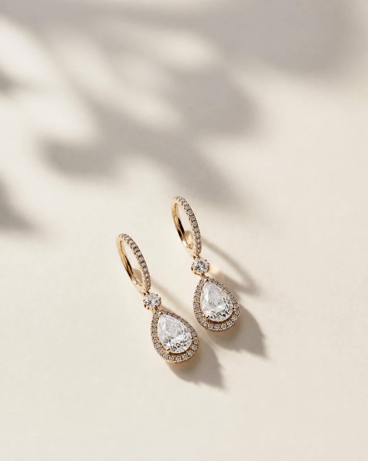 Pair of gold and diamond drop earrings on warm ivory paper